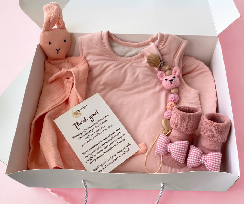 Baby gift set with pink outfit, booties, and toys in a box on a pink background