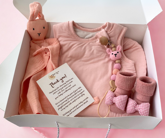 Baby gift set with pink outfit, booties, and toys in a box on a pink background