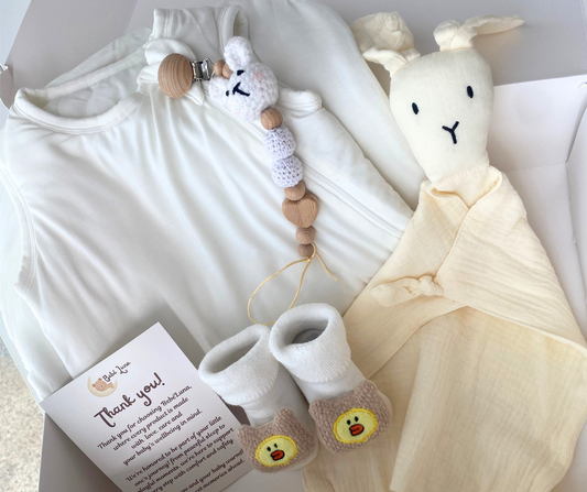 Baby care products including a plush toy, booties, and a card on a white blanket.